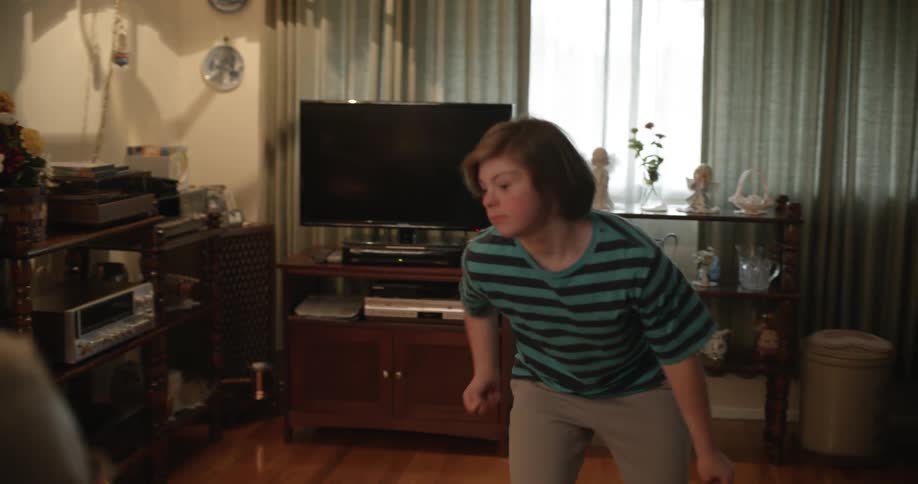 Grandfather reading newspaper looks at granddaughter dancing on the floor in living room at home