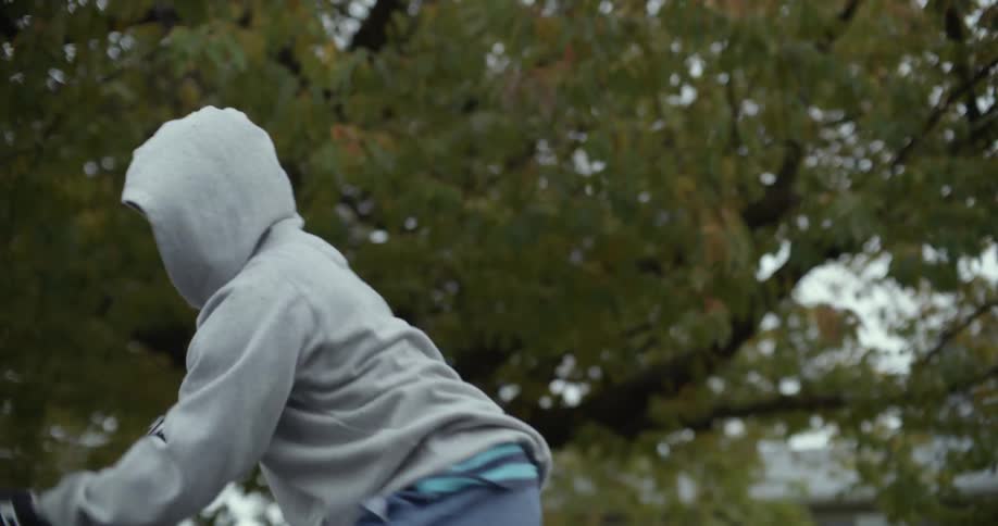 Teenage girl wearing a hoodie practices with hockey stick near tree