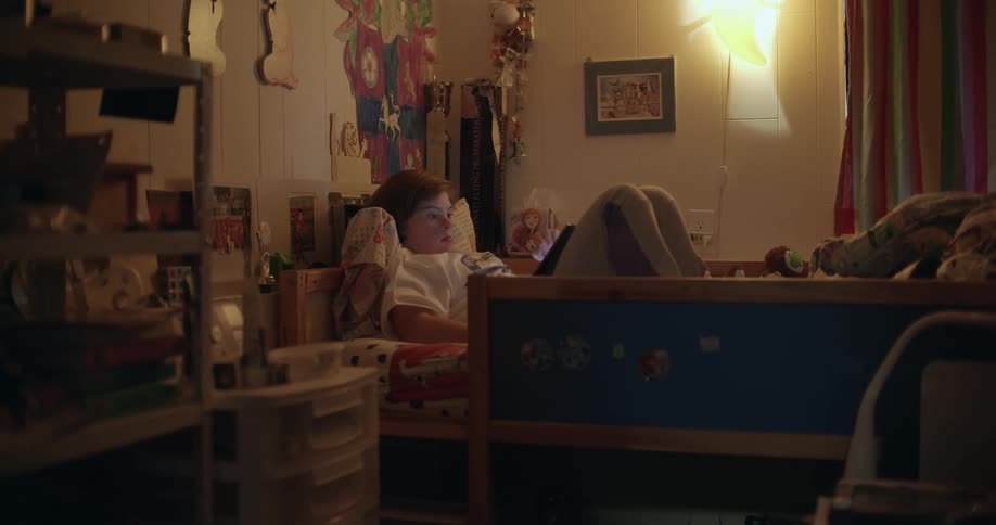 Young girl laying in bed using a tablet in a dimly lit bedroom at home