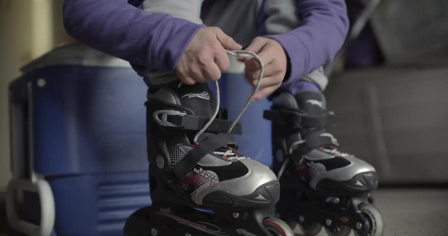 A person ties the strings on their roller skates while sitting atop a cooler
