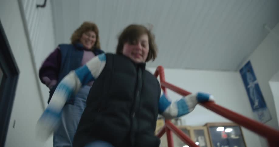 Mother smiles and slowly follows excited teenage daughter down stairs