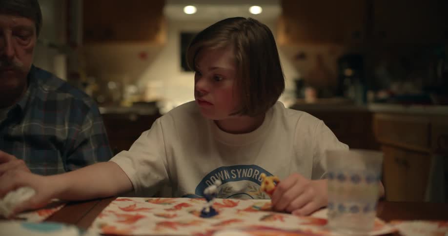 A girl with downs syndrome plays with toys at the table and then takes a wrapper from her dad