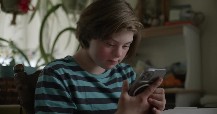 Girl with black and turquoise stripped t shirt sits at table using smartphone in living room at home