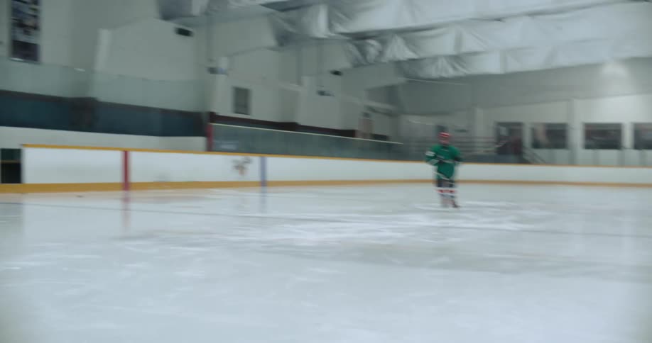 A hockey player hits a puck across the ice of an ice rink