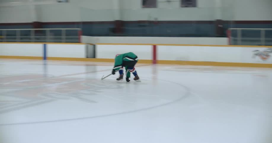 Hockey player practices with hockey stick in rink as another person watches