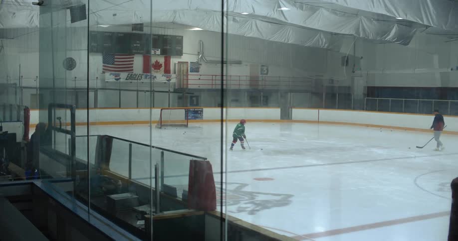A girl is moving a hockey puck around a rink while a coach watches