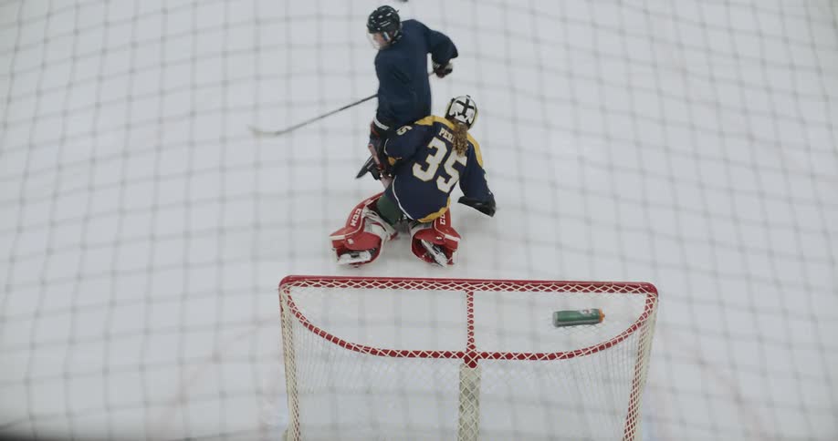 Hockey players try to get pucks into goal past goalie during practice