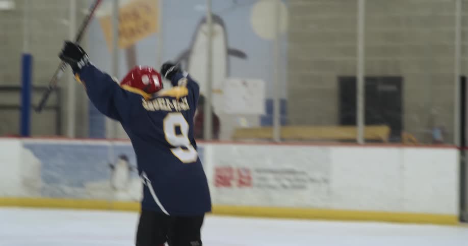 A hockey player hits a puck and raises their arms to celebrate