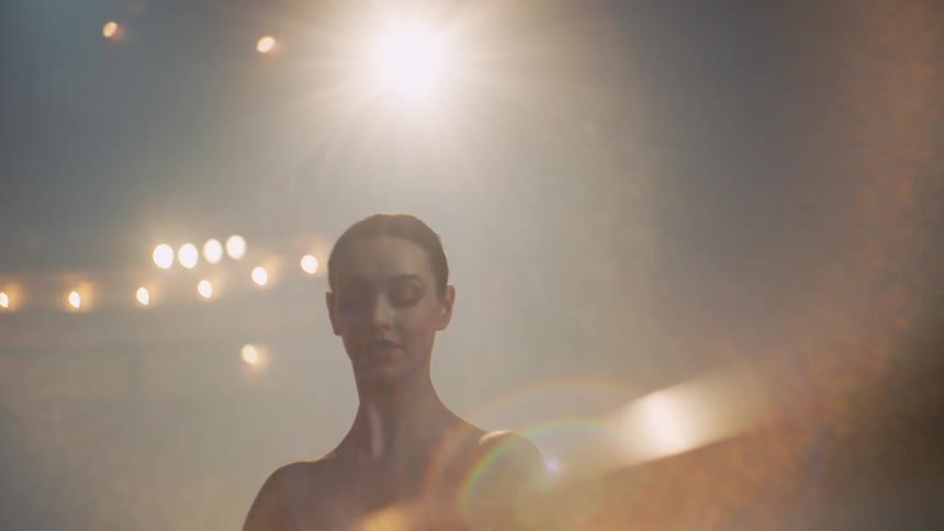 A ballerina is doing her stretches and dance poses on a bar on a stage