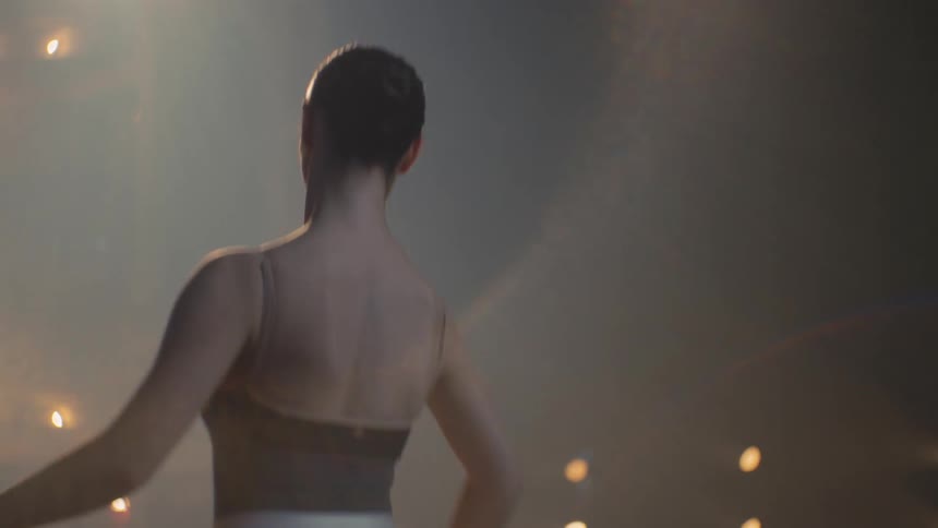 Ballerina practices with freestanding bar under theater lights