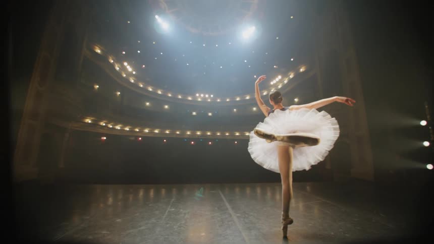 Ballerina dances along on stage in empty theater