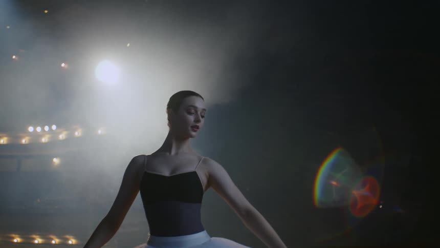 Ballerina practices on stage near freestanding bar in theater
