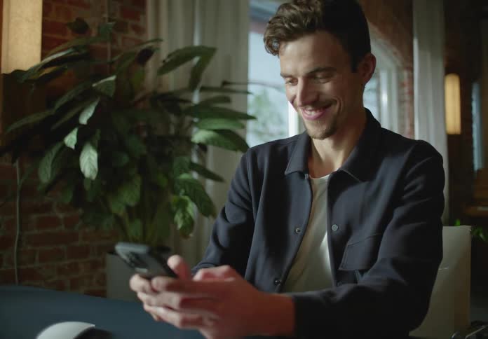 A man laughs while texting on his phone while at his desk in the office