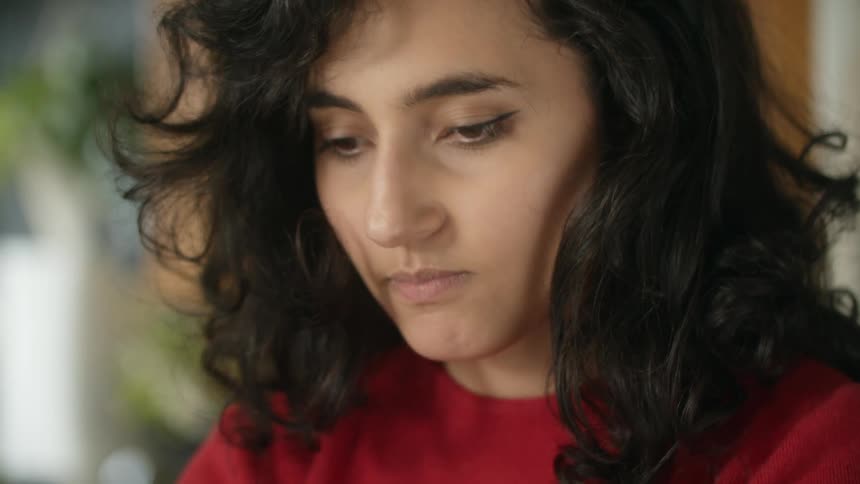 Woman with black wavy hair and red sweatshirt looks down nodding and being surprised in the kitchen