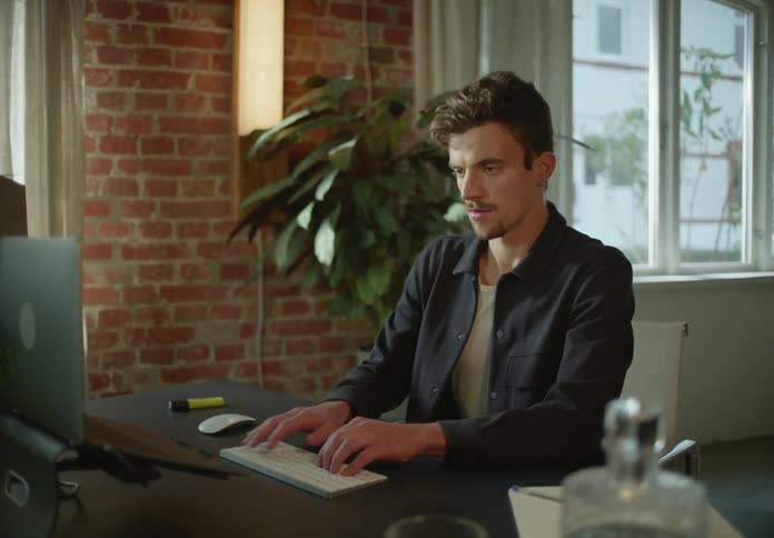 Man sitting at a desk at home typing on a white computer keyboard