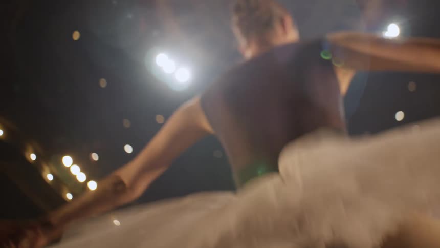 A ballerina dances under bright lights in an auditorium
