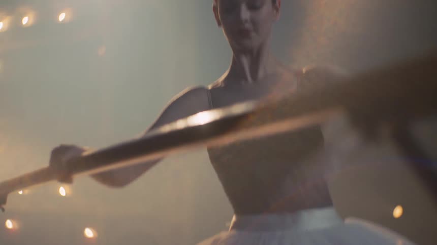 Young ballerina practices ballet poses on a stage under a spotlight