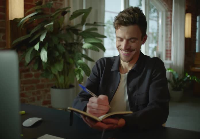 Man working remotely on a zoom call jotting notes in a notebook