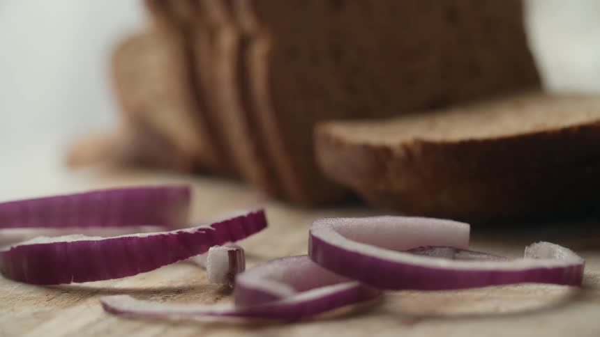 Onion pieces falling on a cutting board near some bread