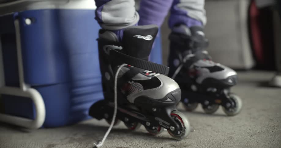 Young woman puts on rollerblades while sitting on ice chest in garage