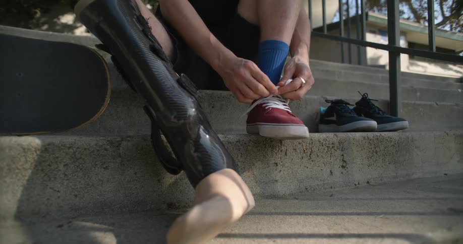 Man pushes sneakers next to another man with a prosthetic leg who is lacing up his sneaker
