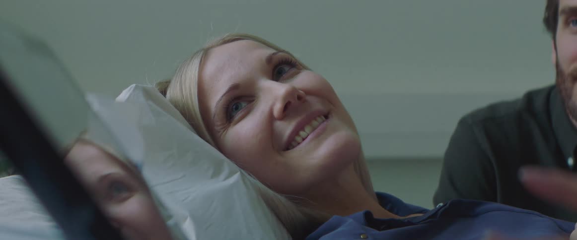 Happy female looking at a screen in a doctors office as husband sits nearby