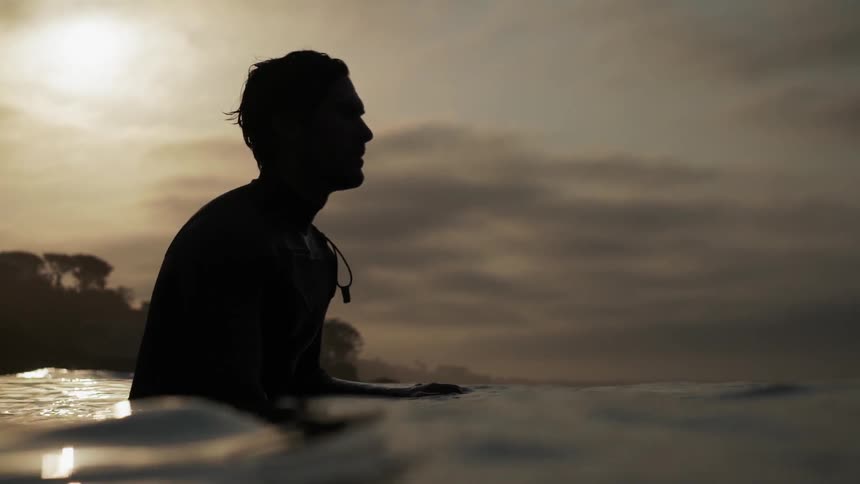 A person sits on a surfboard near sunset