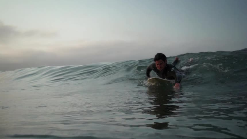 A man rides a surfboard near dusk