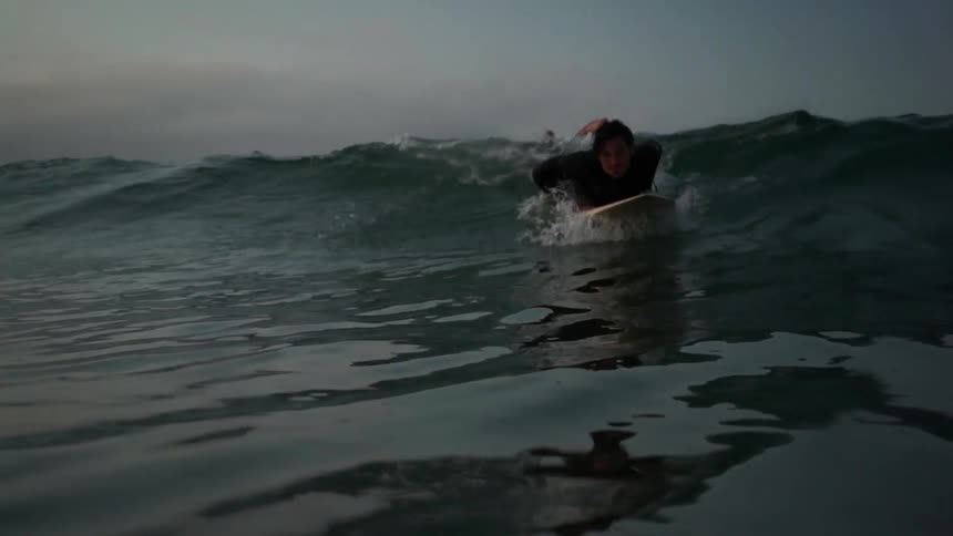 A man surfs in an ocean at dusk