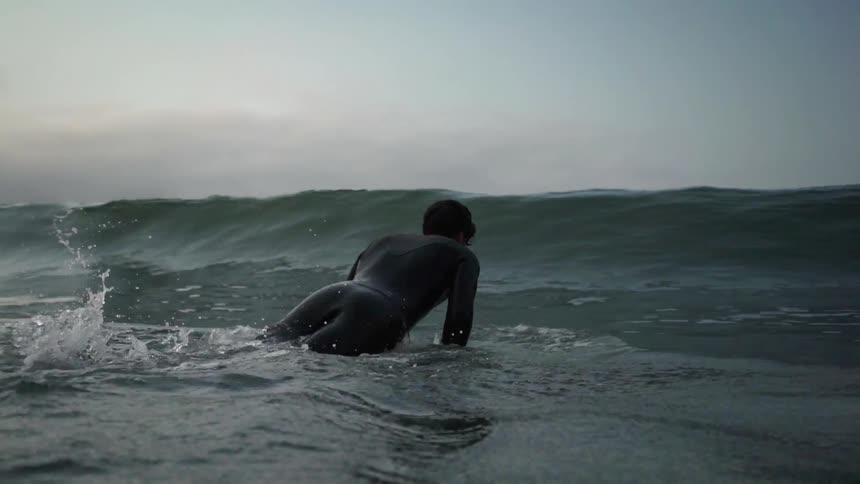 A man rides a surfboard into a wave