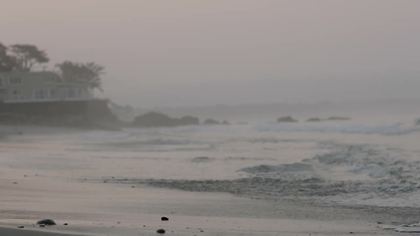 Waves crash against the shore on a foggy day