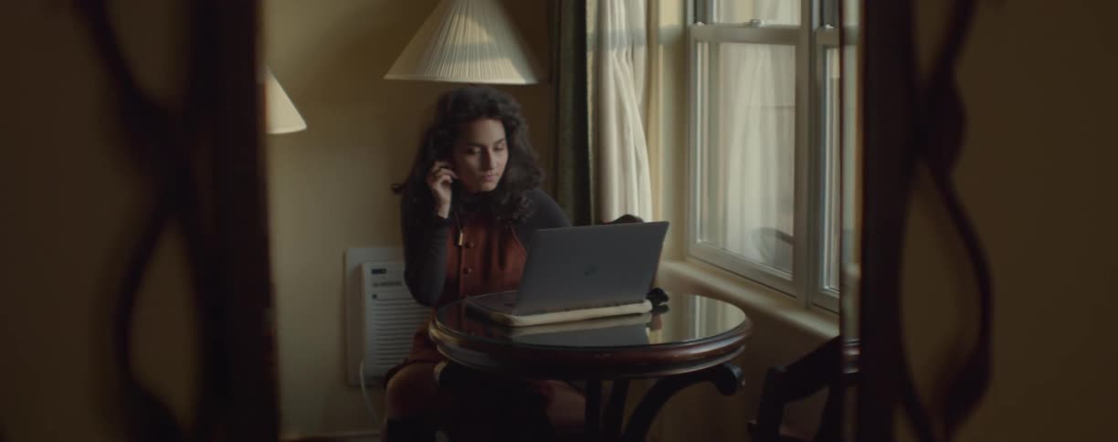 A woman is sitting indoors and on a laptop
