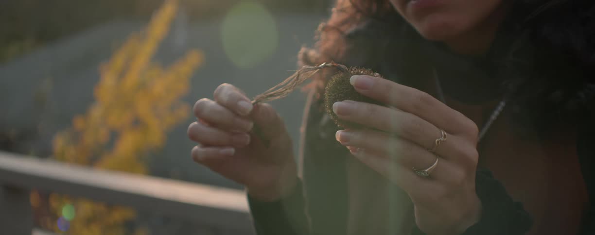 A woman stands outside and holds a round object with a string attached to it and examines it