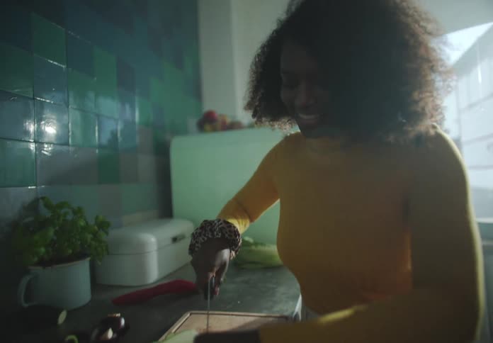Woman stands at counter in kitchen chopping vegetables asman moves around in backgorund