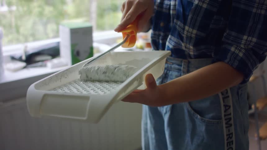 Person coats roller with white paint in paint tray