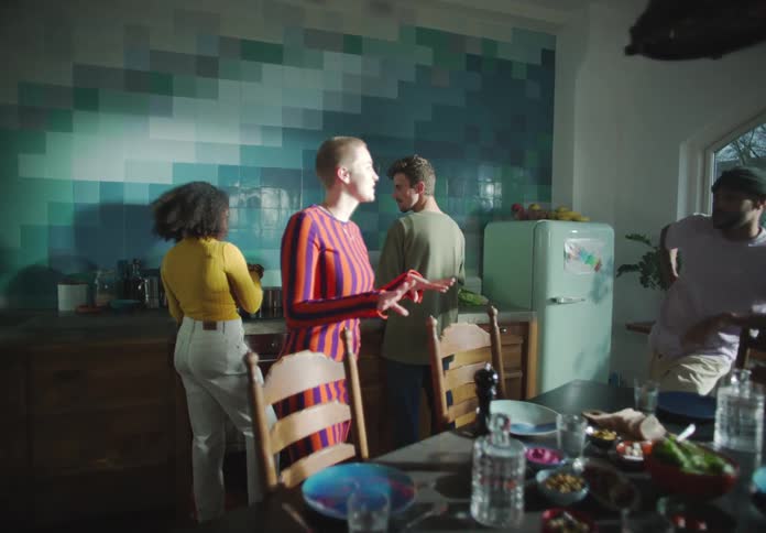 A group of friends talking to each other around dining table and cooking in the kitchen