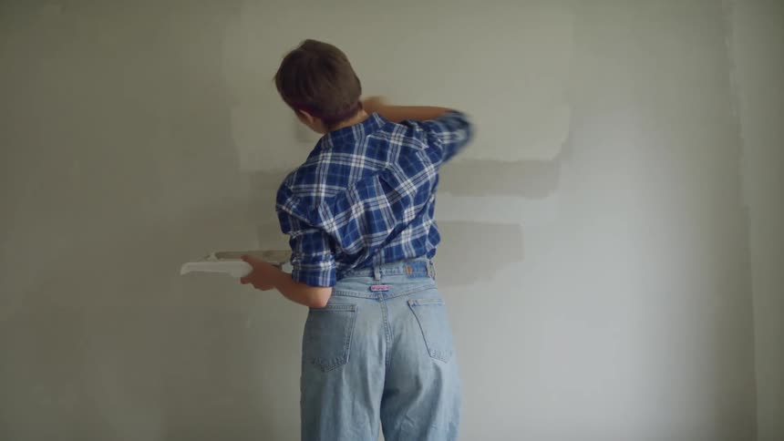A woman is rolling paint onto a wall in a room