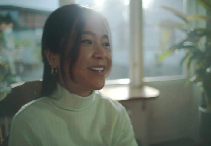 A woman sits at a table in a house and smiles