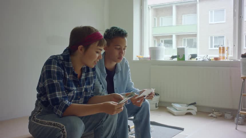 A couple look at paint swatches while sitting in an empty room in their apartment