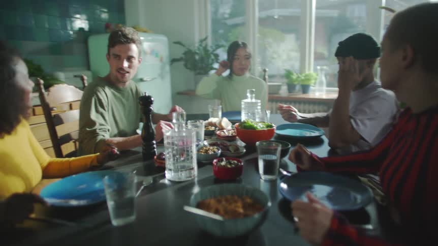 Friends sit talking and eating at table in the kitchen