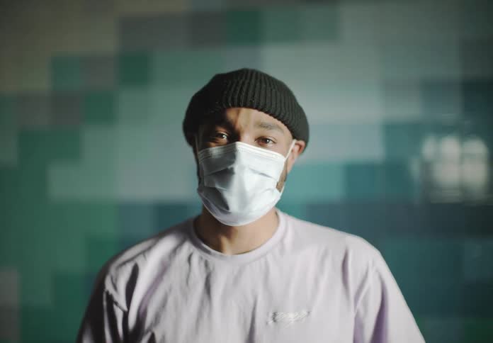 Man with black beanie white mask and sweatshirt looks at camera smiling