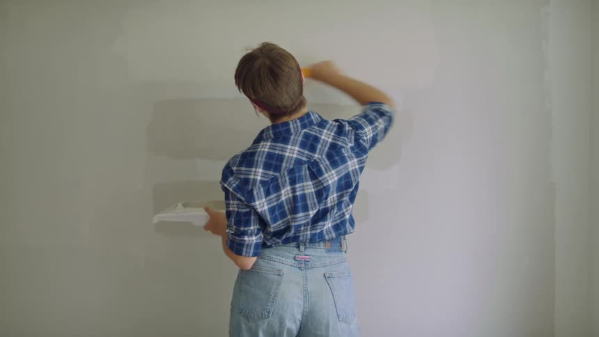 Woman with short hair blue plaid shirt and jeans paints wall white