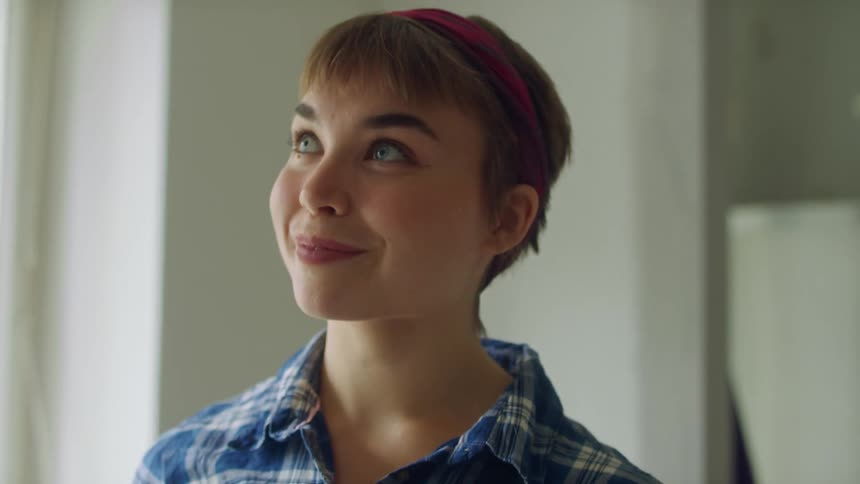 Woman with short hair blue plaid shirt paints wall white in room