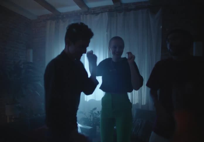 A group of people dance together under flashing lights in a dimly lit room