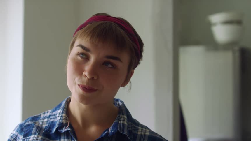 A woman tilts her head and smiles as she contemplates and looks at something in her home