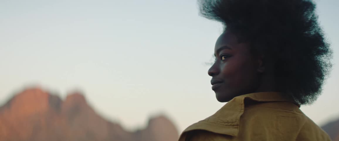 Female fashion model stands outdoors with mountains in the background
