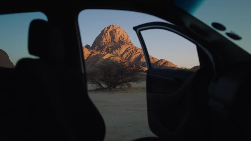 View from a car with door open of large rock formation in desert