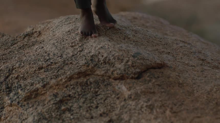 Woman walks barefoot over reddish stone ground in the desert