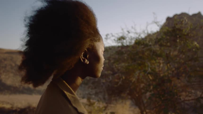 A young woman with afro walking and looking around at a desert landscape at dusk
