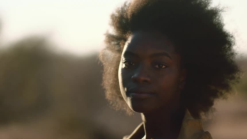 Sun flare portrait of a young black woman with afro at sunset turning and looking directly into the camera